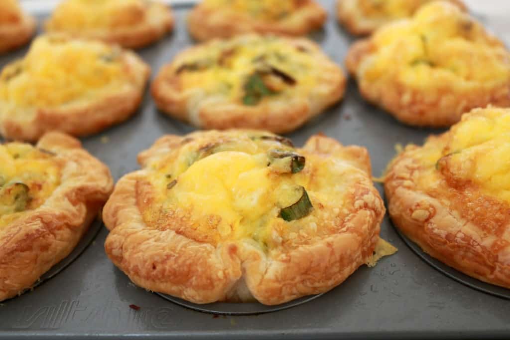 A muffin tray of baked mini pastry quiches filled with ham and corn