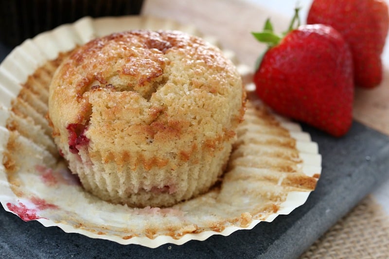A close up of a muffin made with strawberries, banana and yoghurt with its paper case peeled back