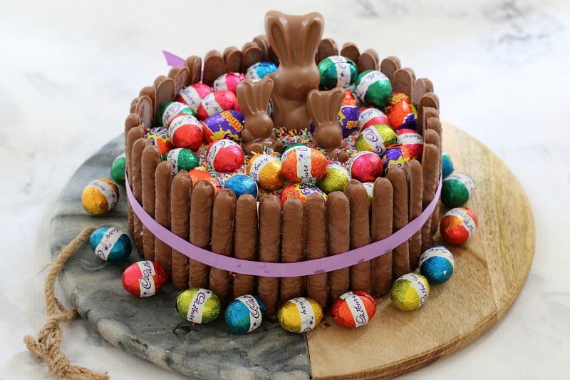 An Easter cake hack made with a store bought mud cake and decorated with chocolate finger biscuits, Easter bunnies and Easter eggs. 