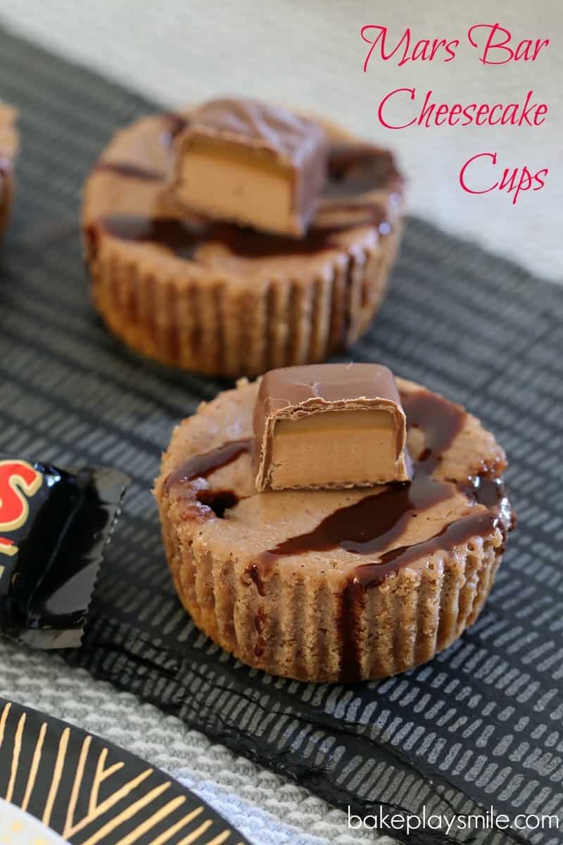 Two individual Mars Bar cheesecakes, drizzled with chocolate sauce and a cut piece of Mars Bar on top,