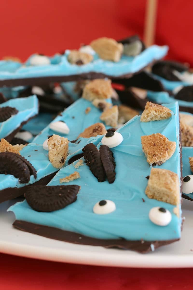 A close up of chocolate bark wedges, topped with a layer of blue candy, with broken Oreo and chop chip biscuits and edible eyes to decorate