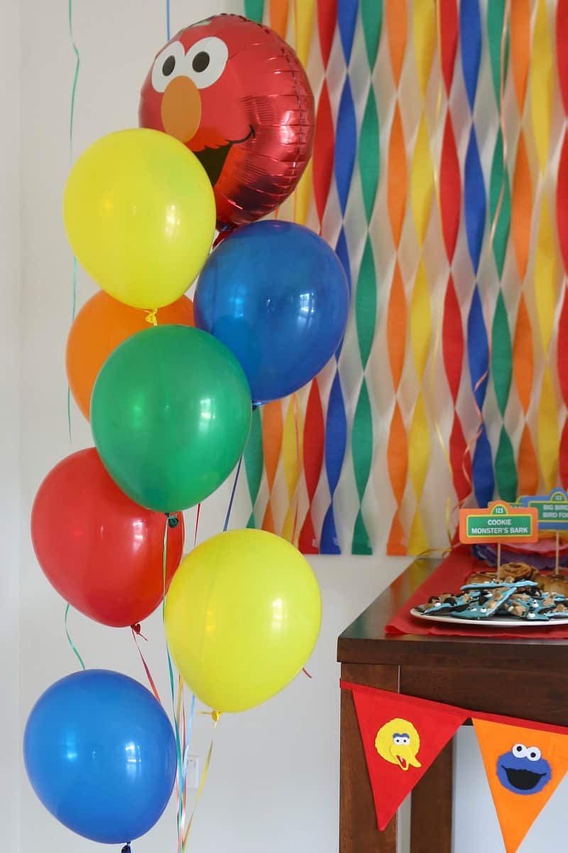 Blue, green, red, orange and yellow balloons in front of colourful streamers and party food