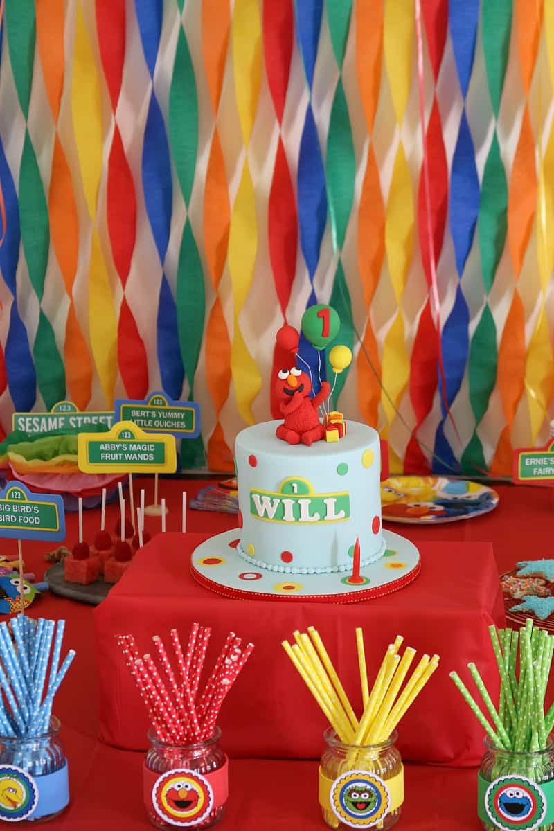 A Cookie Monster birthday cake surrounded by party food and colourful decorations 