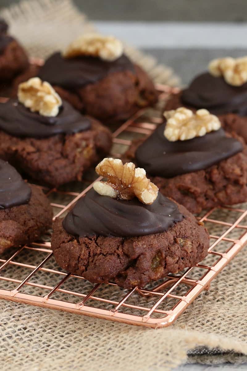 Biscuits au chocolat garnis de chocolat noir fondu et d'une noix sur une grille en fil de cuivre.