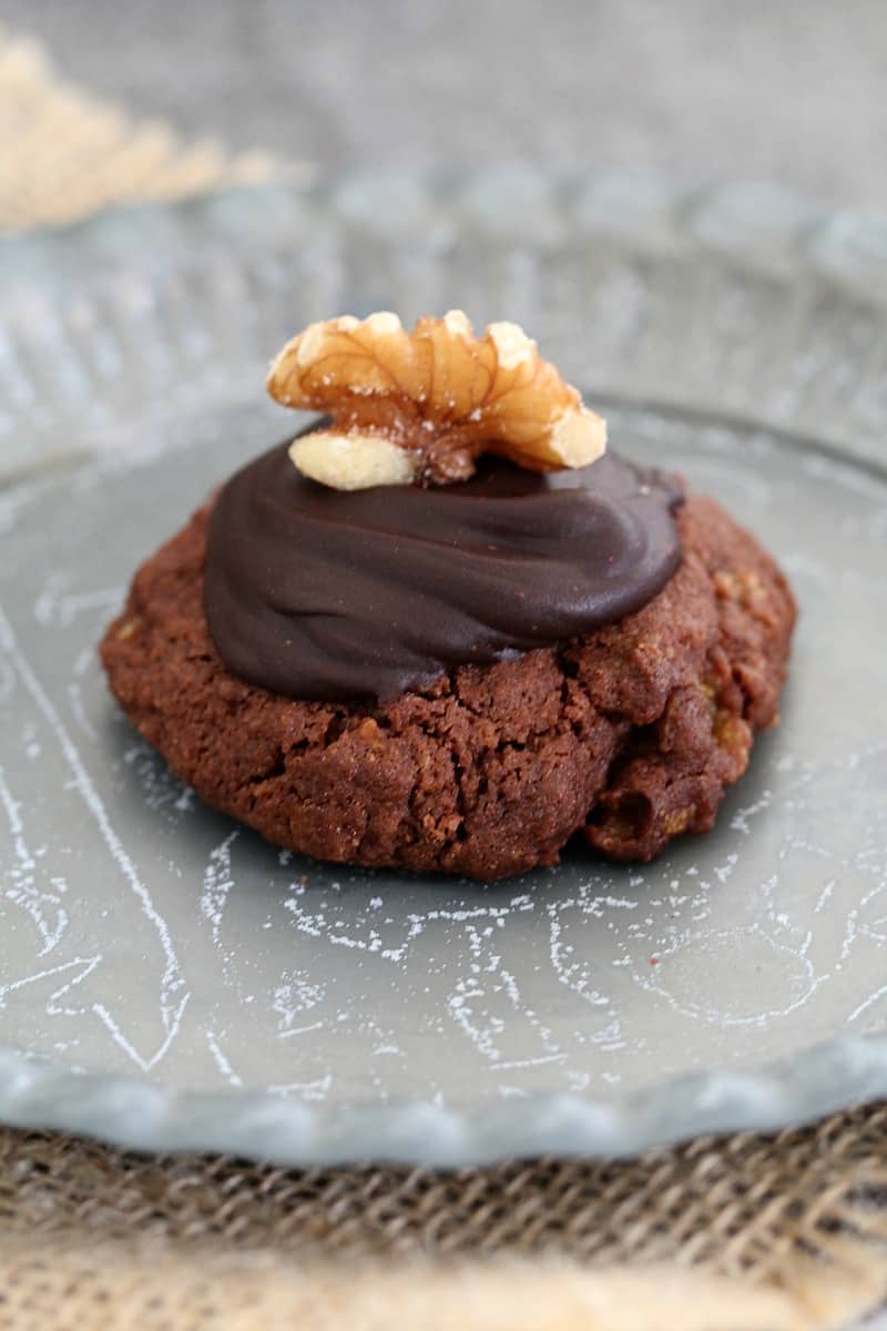 A chocolate biscuit made with cornflakes topped with icing and a walnut on a metal plate.