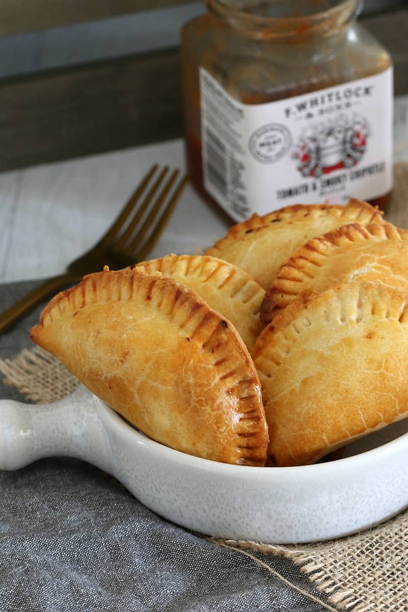 Five empanadas in a white serving bowl, in front of a jar of relish