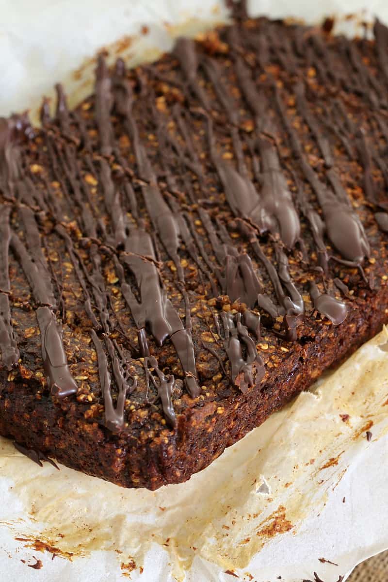 A close up of a slice made with dates and oats and drizzled with dark chocolate, sitting on baking paper