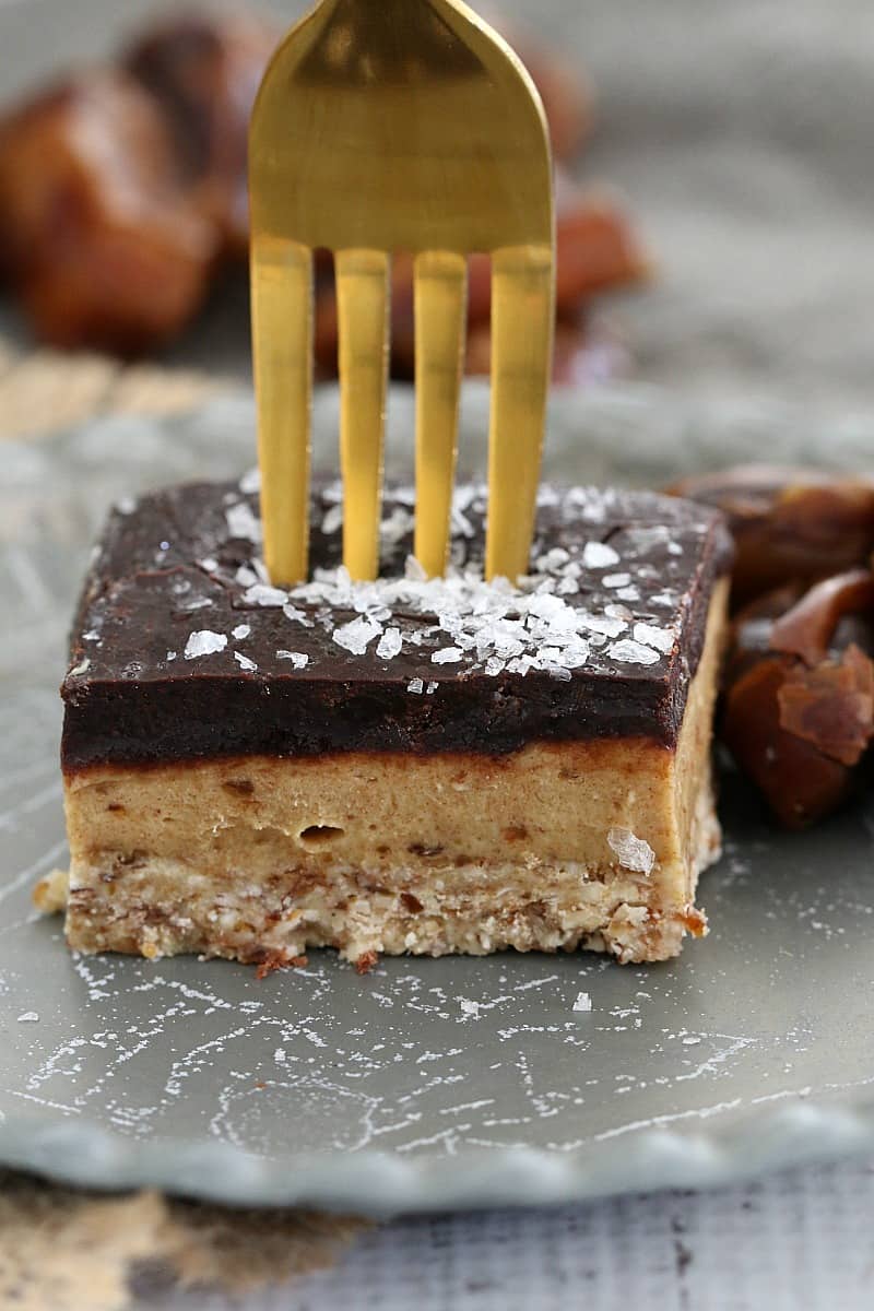A gold fork standing up in a three layered square of slice and sprinkled with sea salt