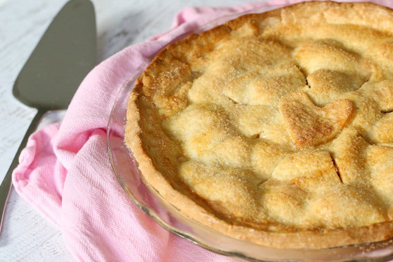 A pie dish filled with Apple Pie on a pink tea towel