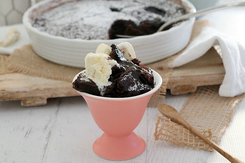 A pudding dish of chocolate pudding behind a  pink parfait dish with one serve topped with ice cream