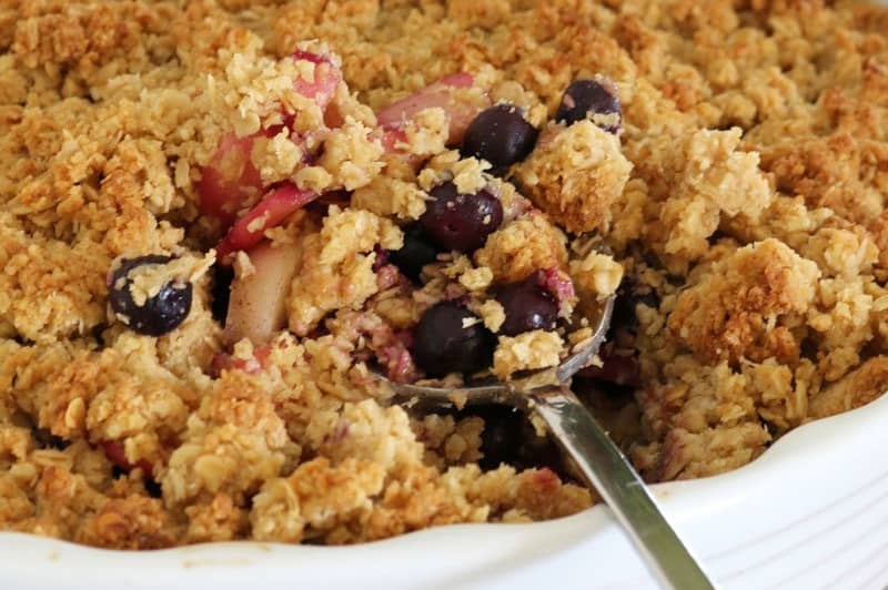 A spoon going into a serve of a dessert made with apple and blueberries and a crumble topping