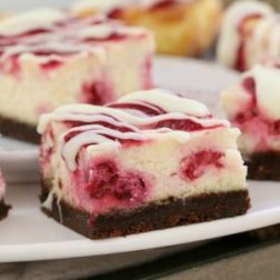 A close up of cheesecake squares made with a chocolate base and a white chocolate filling with raspberries swirled through