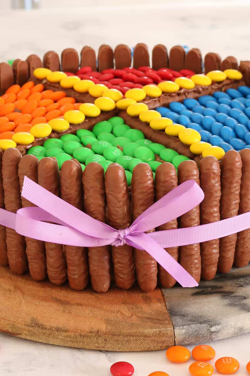 A round cake with chocolate log biscuits placed around the outside, and coloured M&M\'s on top