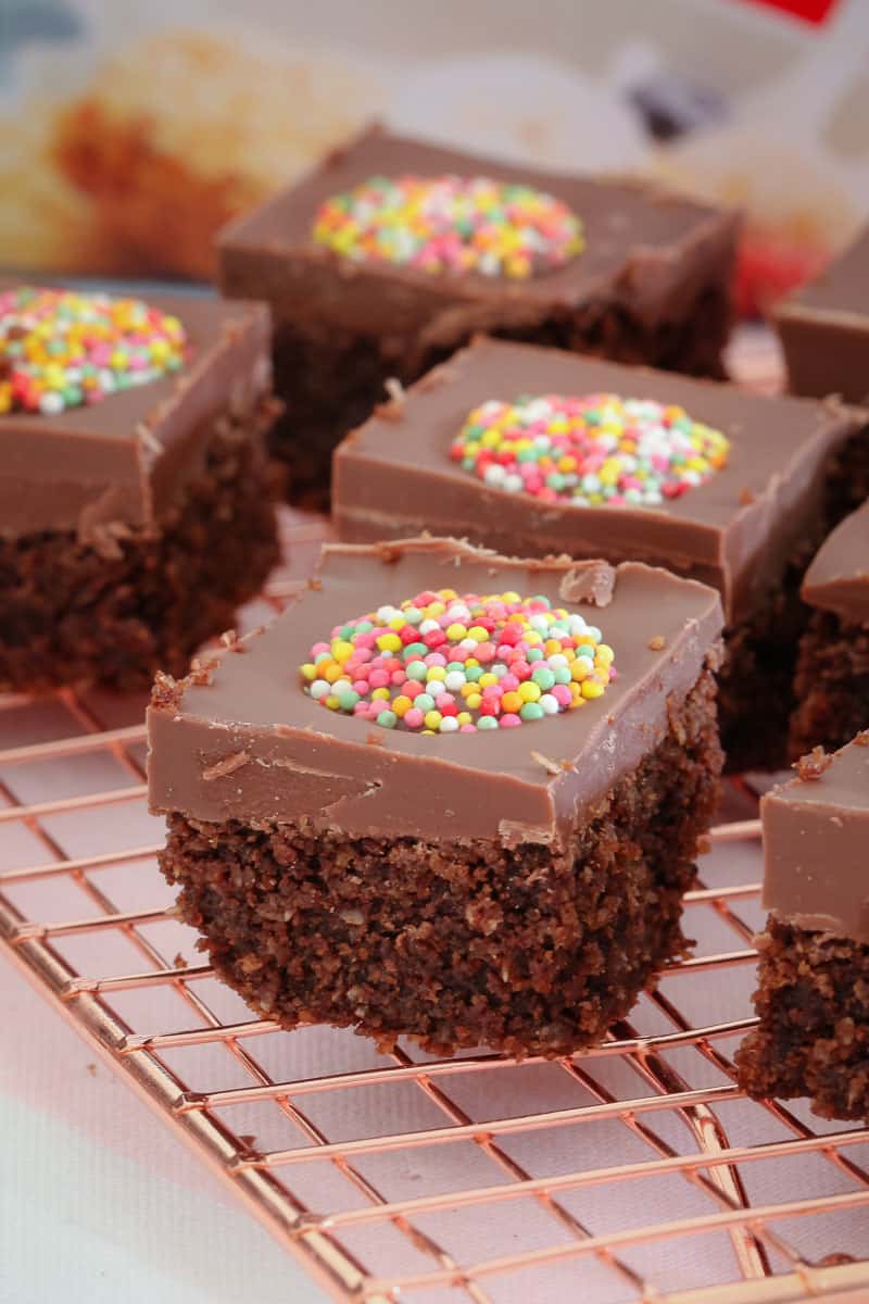 A close up of squares of a chocolate slice, iced with milk chocolate and a coloured Freckle on top