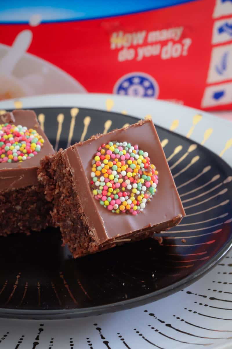 Two squares of a chocolate slice with a milk chocolate topping and a coloured Freckle on top, on a plate
