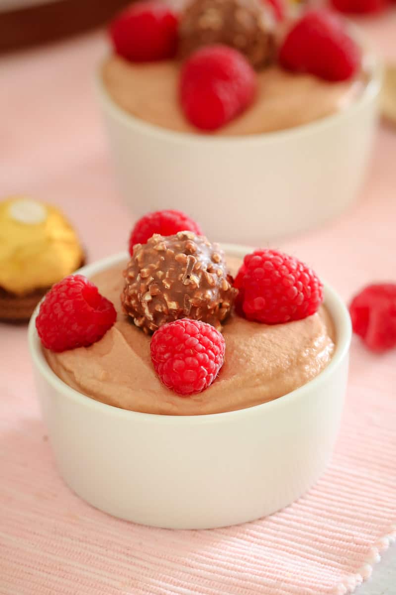 A small white bowl filled with mousse and decorated with fresh raspberries and a Ferrero Rocher