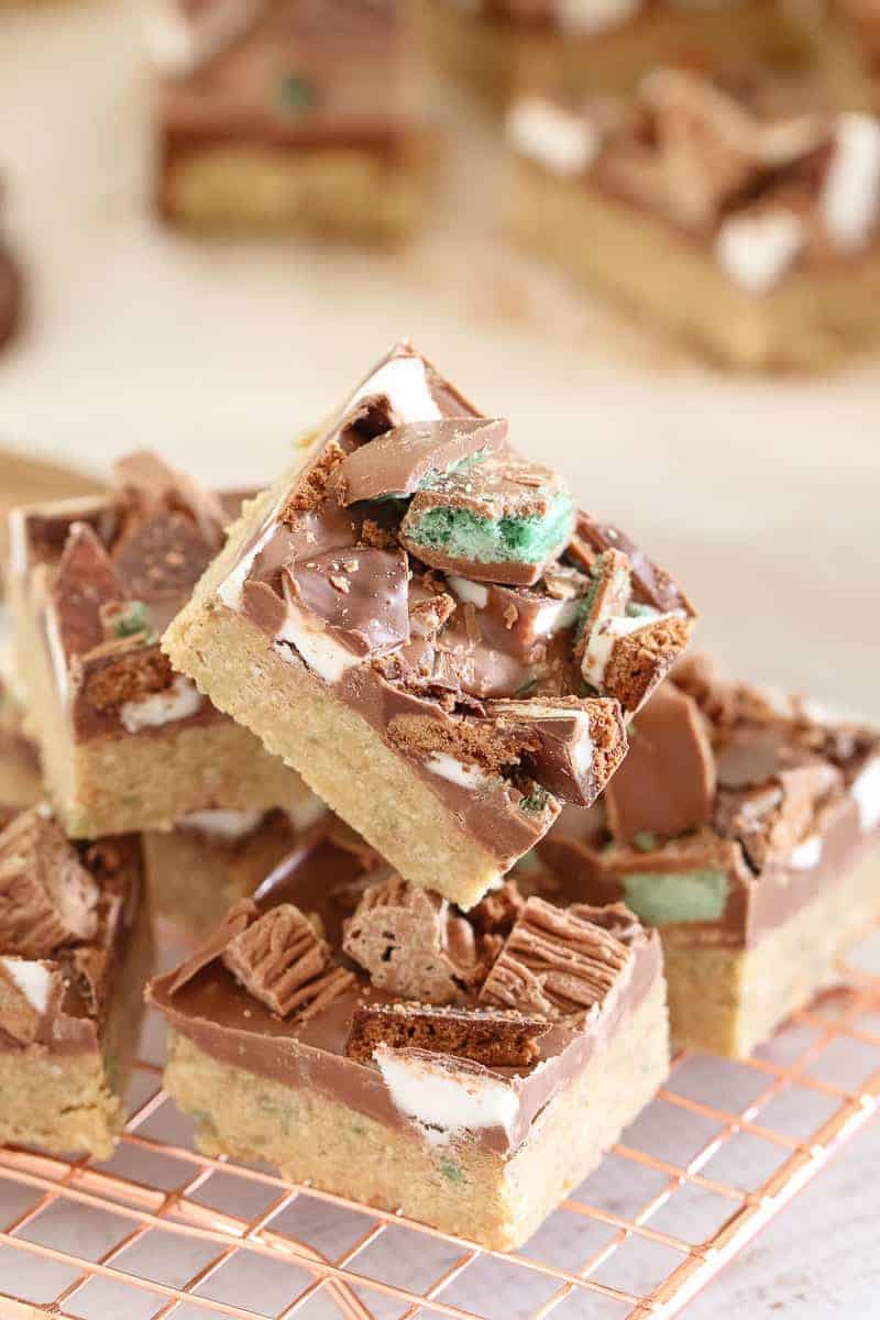 A stack of slice squares with a biscuit base, a layer of chocolate, and chopped peppermint chocolates on top
