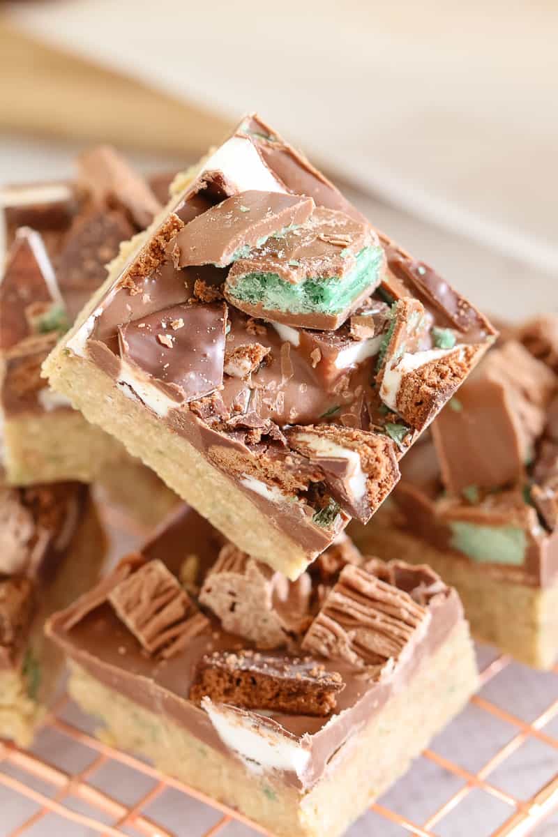 A stack of squares of slice made with a biscuit base, a layer of chocolate, and decorated with chopped peppermint chocolates
