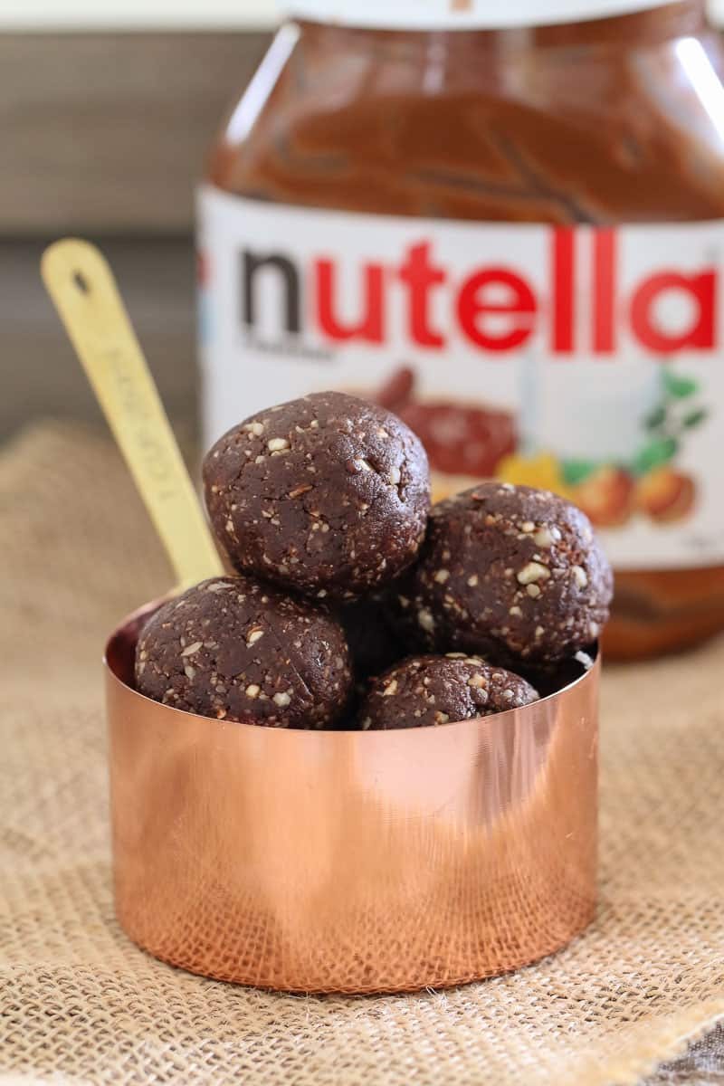 A copper measuring cup filled with Nutella Bliss Balls in front of a jar of Nutella