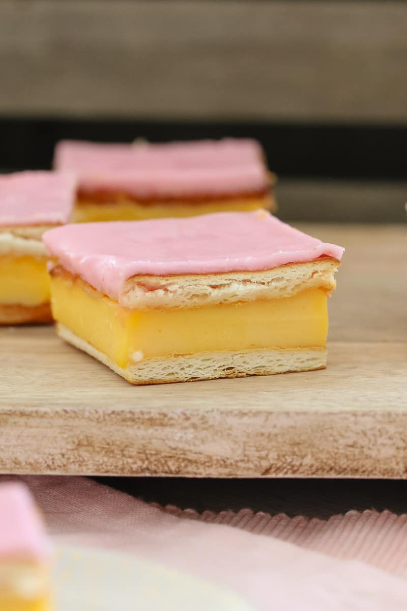 Pieces of slice made with layers of flakey pastry filled with custard and topped with pink icing glaze.