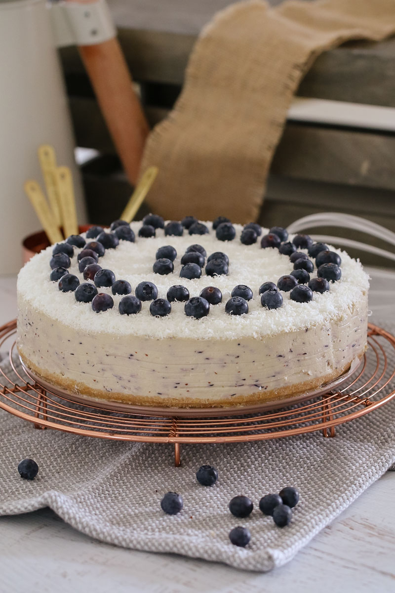A white chocolate cheesecake decorated with blueberries sitting on a copper wire tray