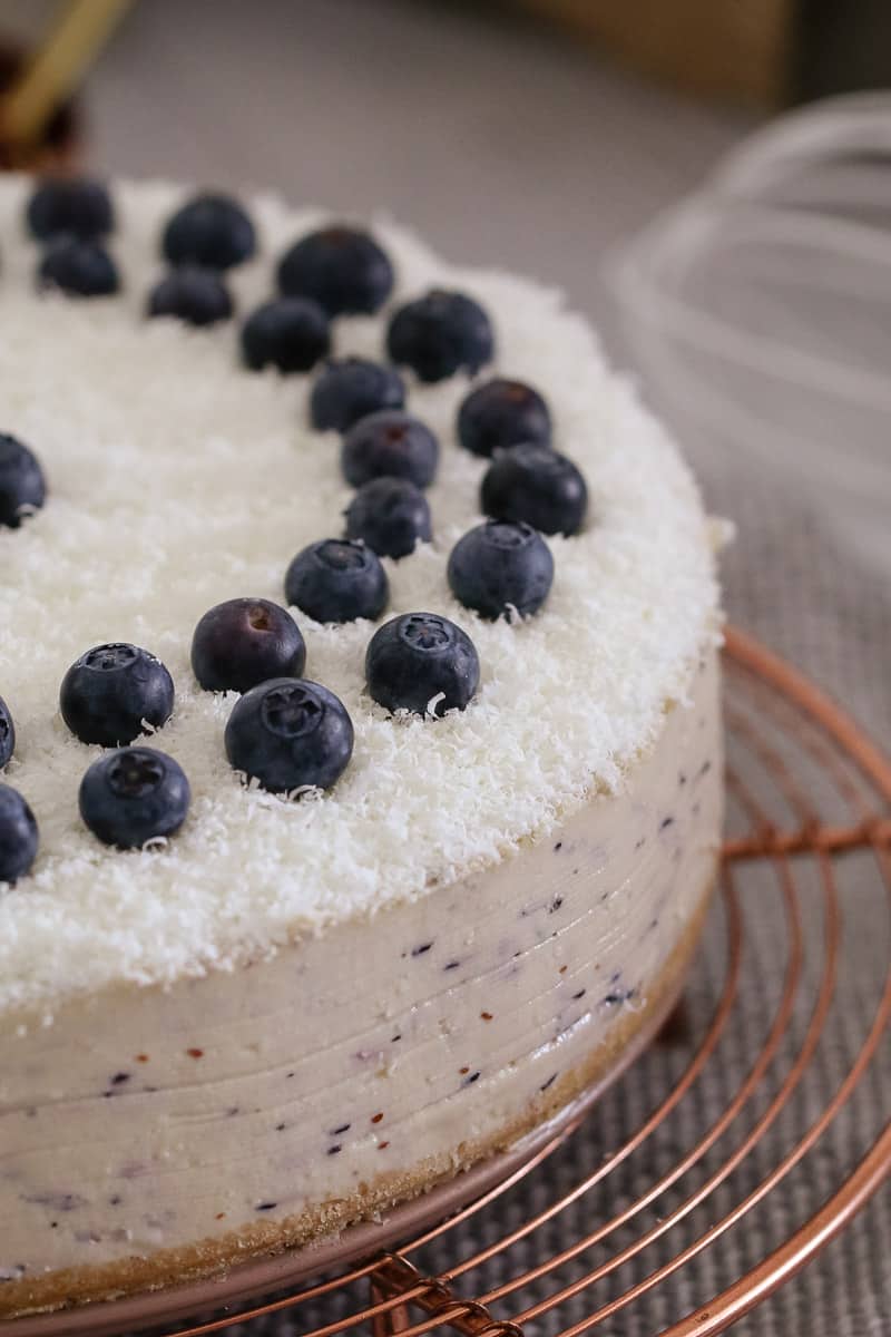 A close up of a white chocolate cheesecake, topped with fresh blueberries and grated white chocolate