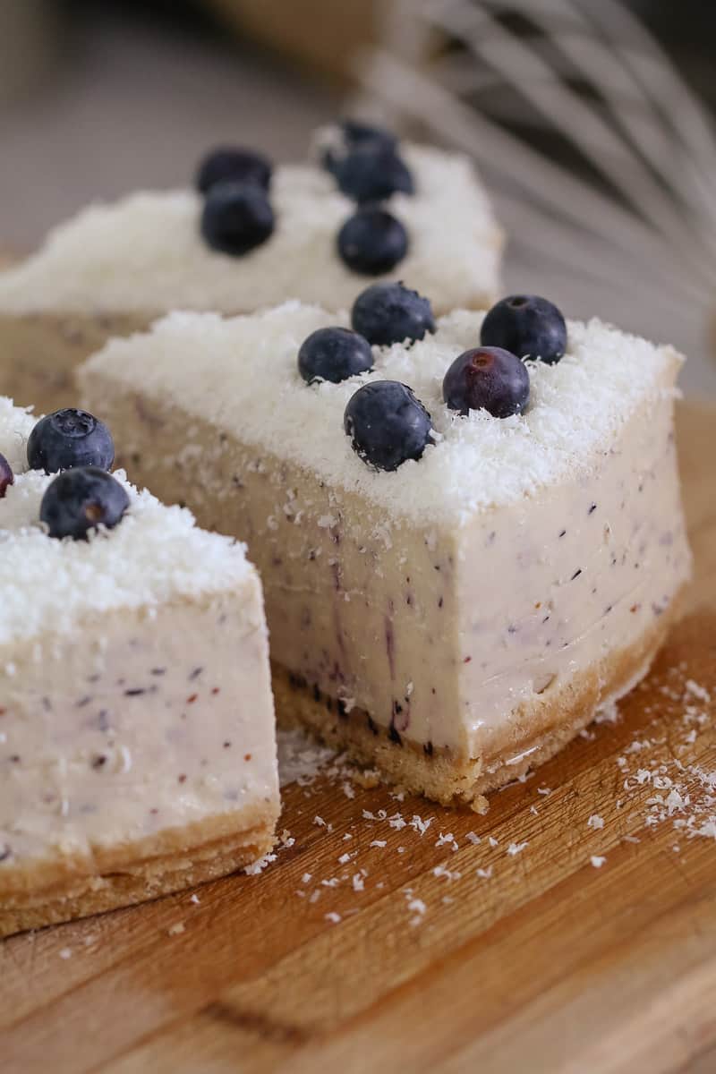 A close up of cut serves of cheesecake with fresh blueberries and grated white chocolate on top