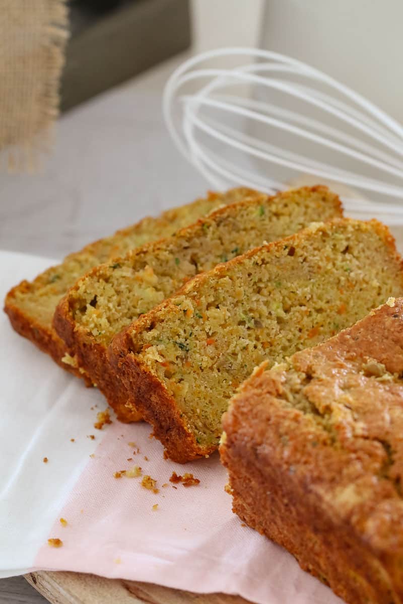 Slices of Apple, Zucchini and Carrot loaf cut and sitting on a bench in front of a whisk utensil