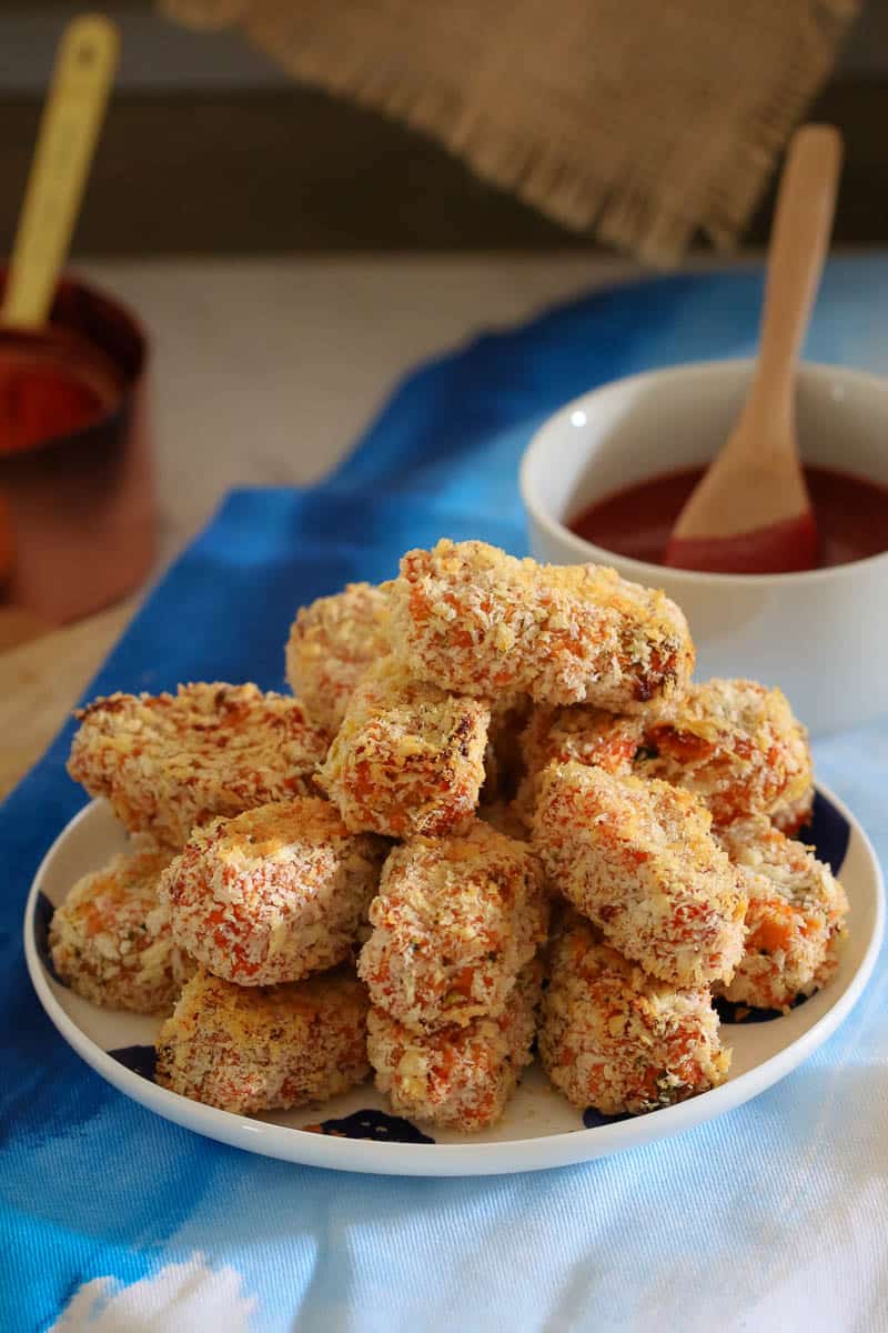 A pile of crumbed veggie nuggets on a plate with a bowl of dipping sauce beside