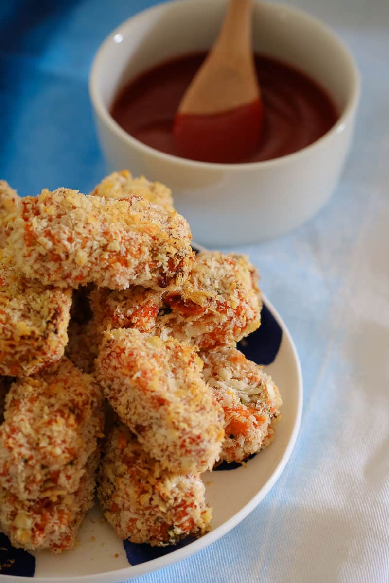 A pile of golden bread crumbed nuggets on a plate next to a bowl of dipping sauce