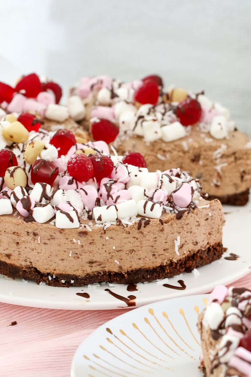 A cheesecake decorated with mini marshmallows, raspberry lollies and chocolate sauce, with one slice removed