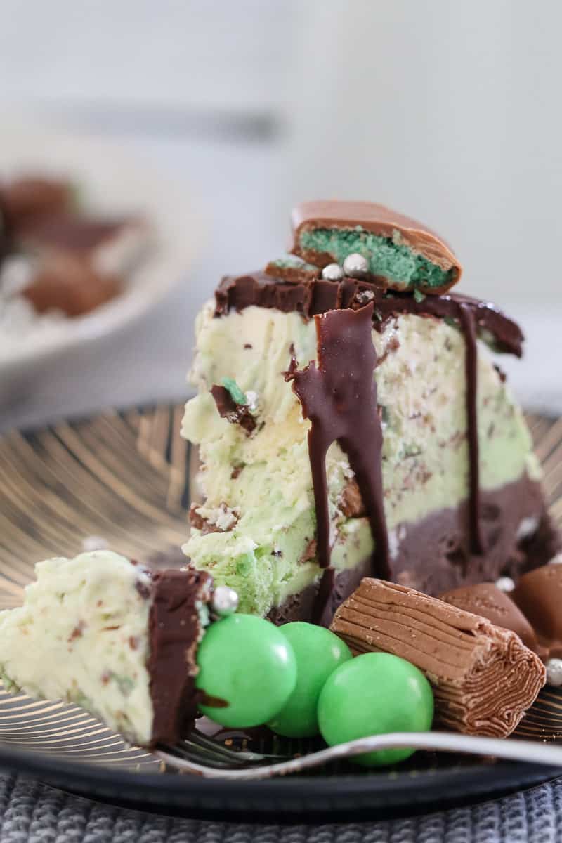 A fork with a piece of peppermint Christmas ice-cream cake with extra peppermint chocolates on the side. 