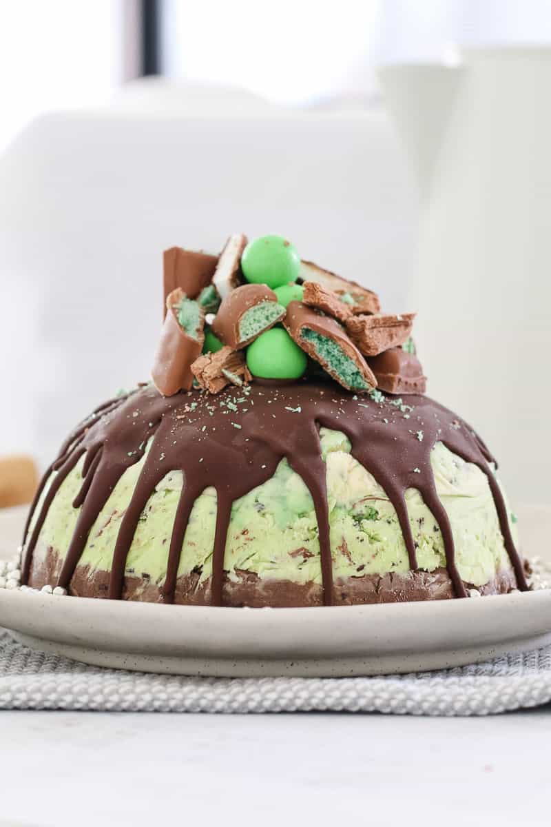 A mint ice cream cake topped with hard shell chocolate and chopped mint flavoured chocolates on top with silver edible balls around the base.