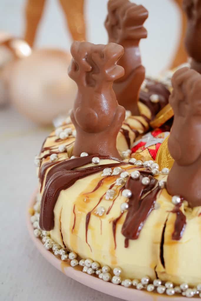 A close up of a chocolate cake drizzled with chocolate and caramel sauce and decorated with chocolate reindeer, Santa\'s and silver baubles