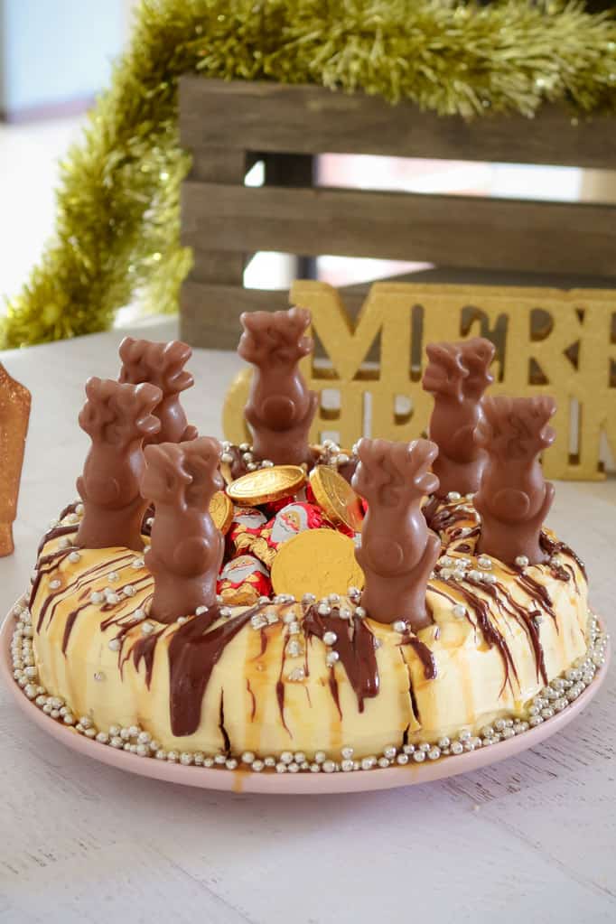 A cake decorated with chocolate reindeer, Santa\'s and silver baubles, in front of Christmas decorations