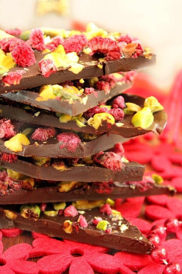 Pieces of chocolate bark topped with pistachios and dried raspberries stacked on top of each other.