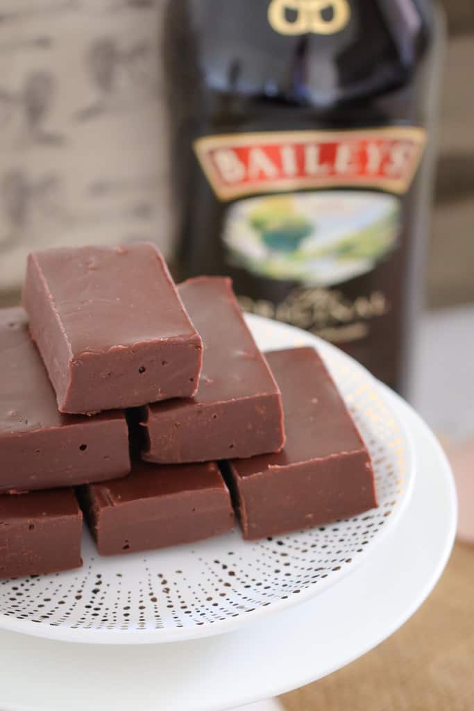 Looking down at a stack of chocolate fudge on a cake plate with a bottle of Baileys in the background