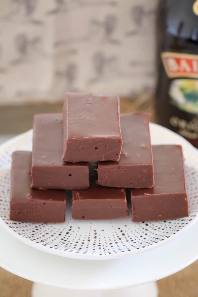 A stack of pieces of chocolate fudge on a white plate in front of a bottle of Baileys
