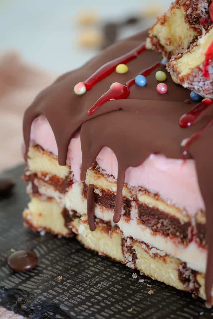 A close up of a layered lamington ice cream cake drizzled with chocolate and raspberry topping and sweets