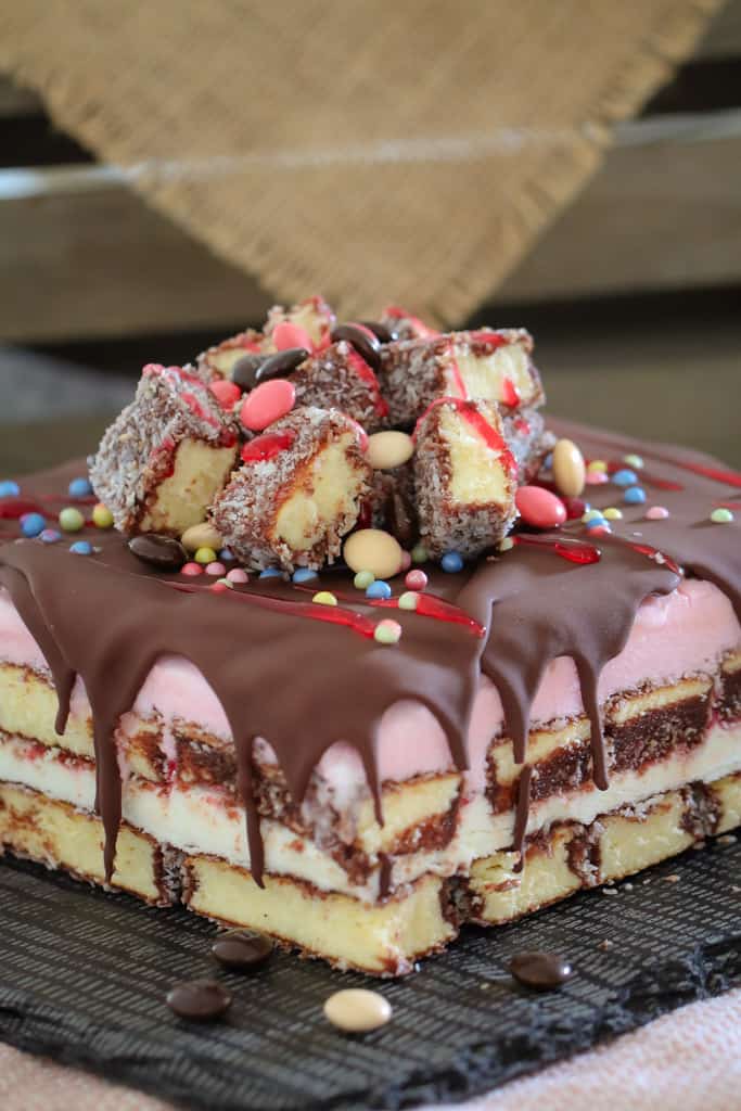 A square lamington ice cfeam cake showing layers, topped with chocolate, raspberry topping and cut lamingtons