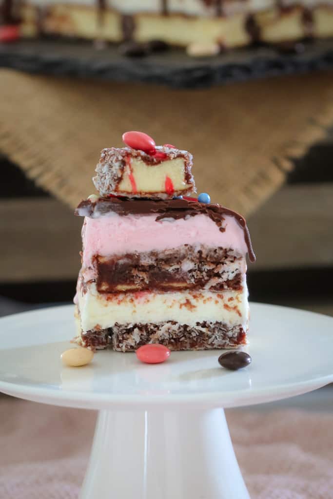 A serve of a layered lamington ice cream cake on a white cake stand