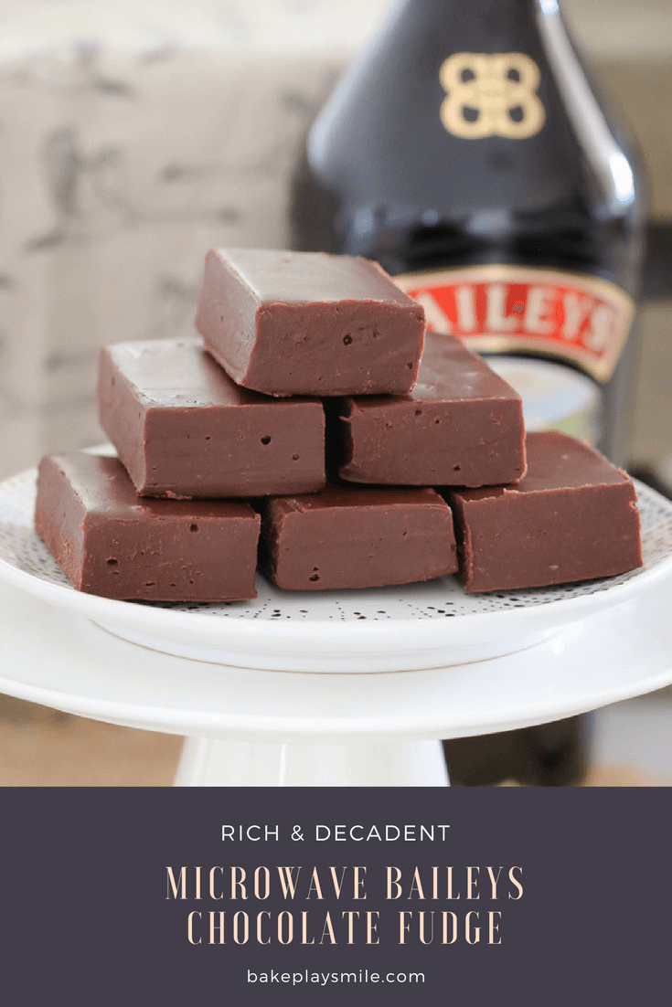 A stack of chocolate fudge on a white cake stand in front of a bottle of Baileys