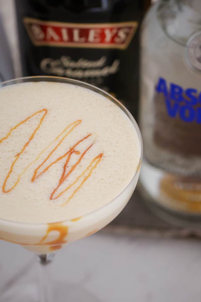 Looking down on a creamy cocktail with caramel swirls beside of a bottle of Baileys and Vodka