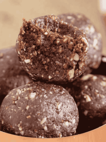 Copper bowl filled with healthy Nutella bliss balls, with one bliss ball on top bitten in half.