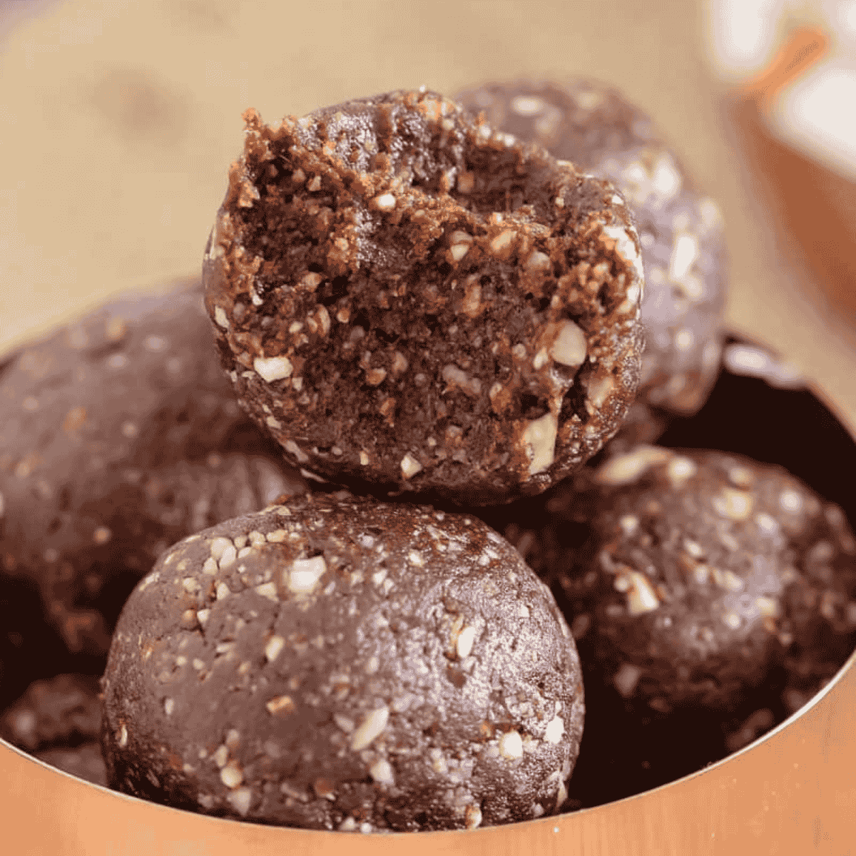 Copper bowl filled with healthy Nutella bliss balls, with one bliss ball on top bitten in half.