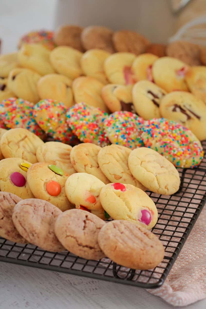 Rows of different types of baked cookies from the famous 100 cookie recipe, cooling on a wire rack