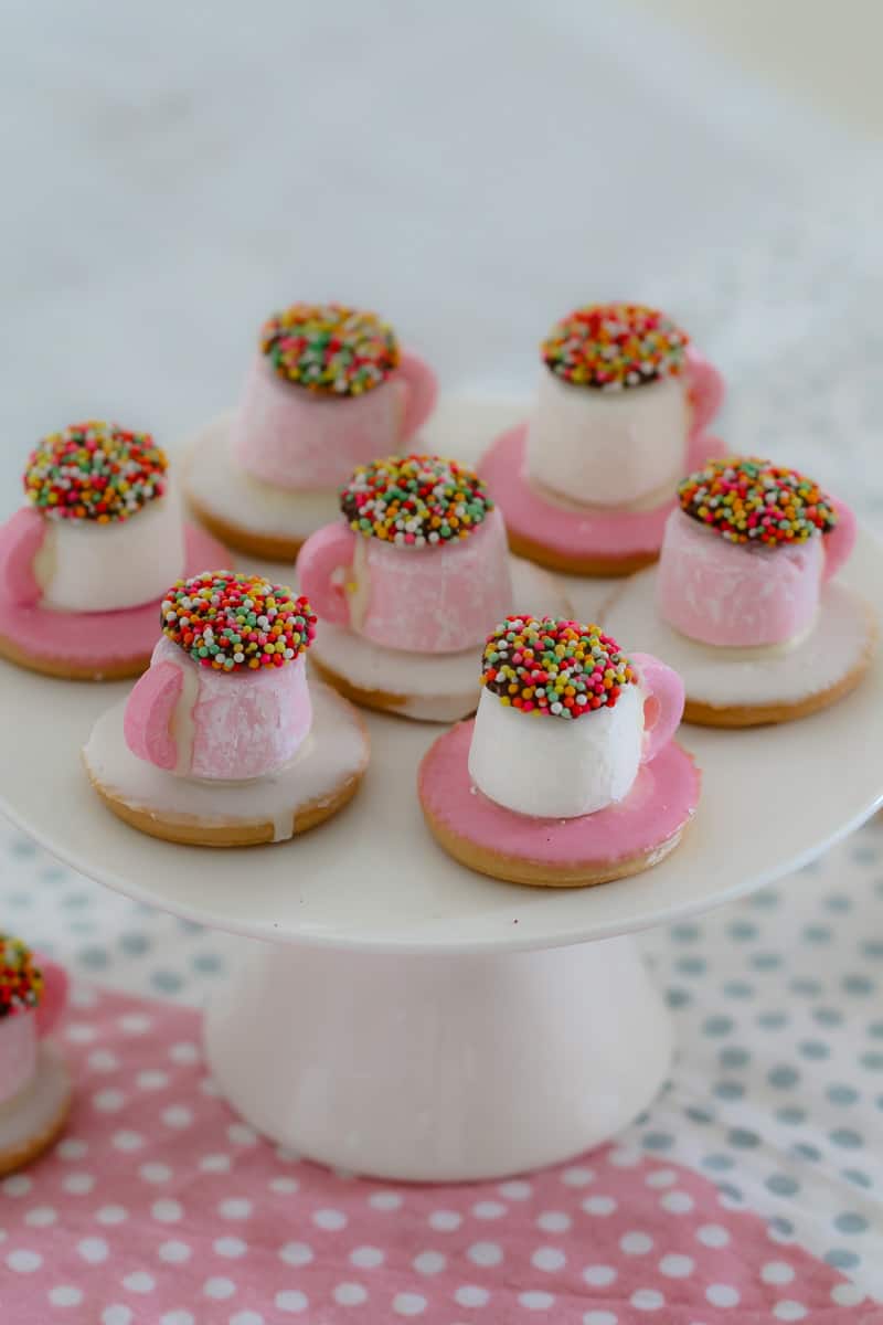 A group of Mini Tea Cups made with a pink iced biscuit, a marshmallow and lollies, on a white cake stand