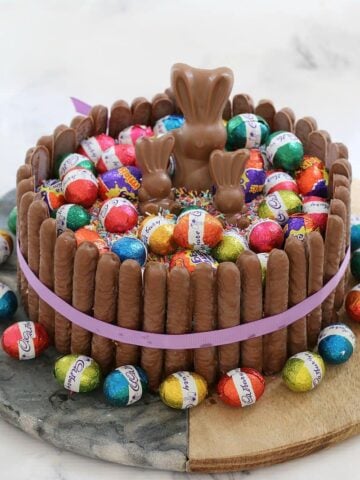 A round cake decorated with chocolate fingers around the outside and topped with chocolate bunnies, mini Easter eggs and sprinkles