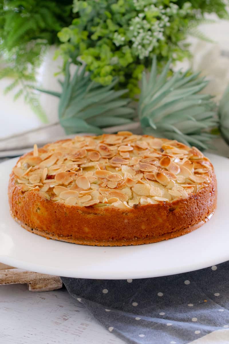A golden butter cake with layers of apple slices and topped with flaked almonds.