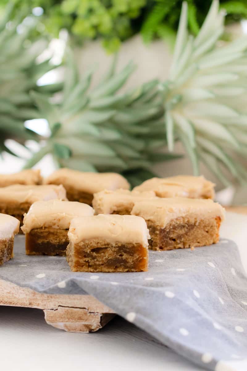 Squares of slice topped with caramel frosting on a blue tea towel